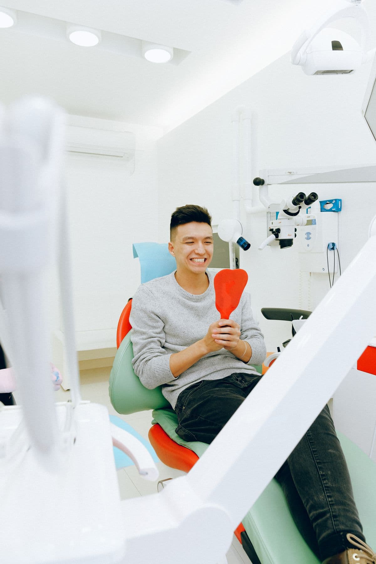 Young man smiling while holding a mirror in a dental chair